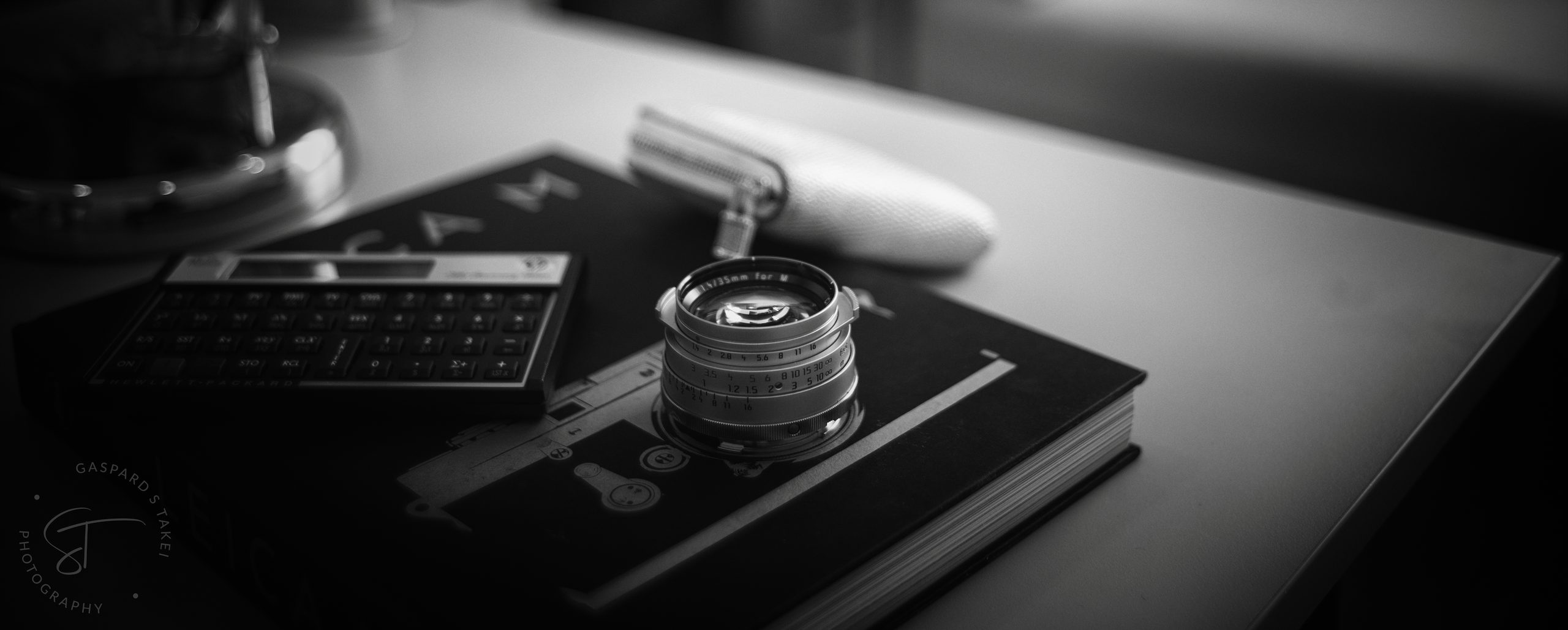 Leica lens, HP calculator and a Leica book on a desk — photo by Gaspard Shinya Takei